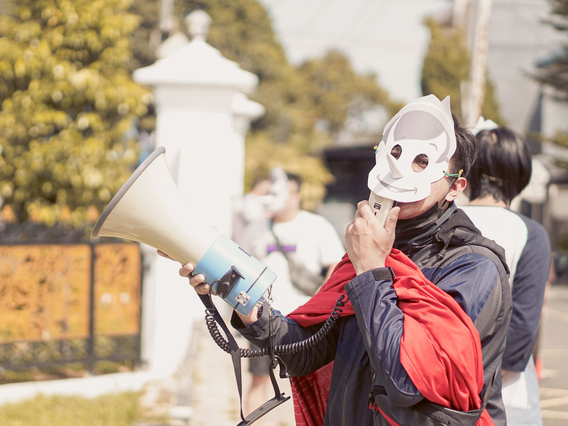 A masked protestor in West Java, Indonesia, using a megaphone during a daytime demonstration.