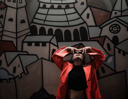Fashionable woman in red jacket striking a pose against a geometric mural.
