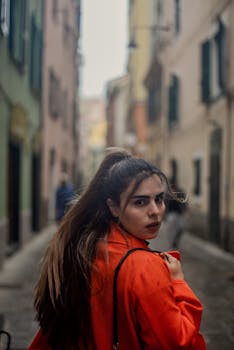 Stylish woman in red coat walking through the narrow alleys of Genoa, Italy. Urban fashion portrait.