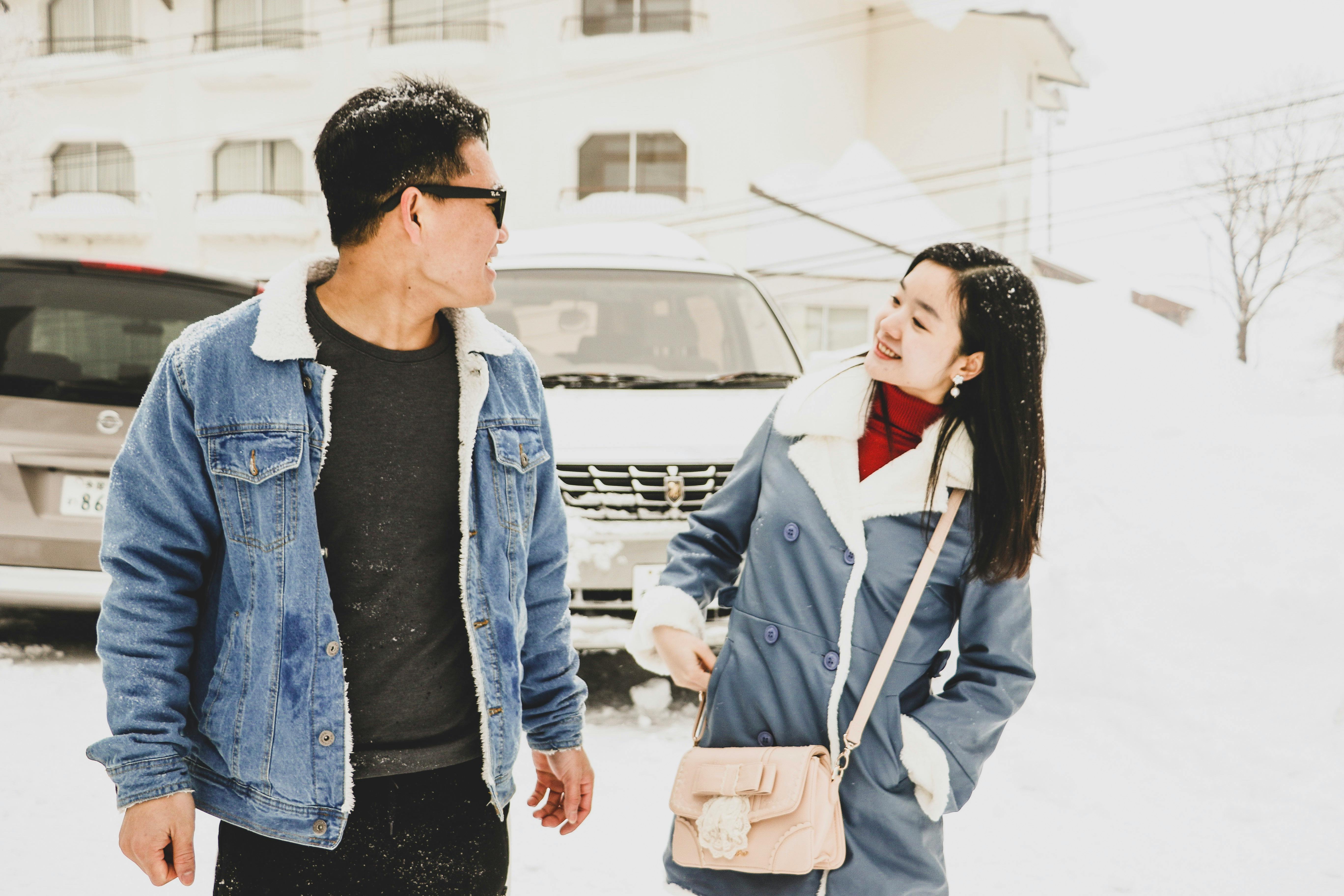 一对亚洲夫妇穿着温暖的冬装，在户外微笑着享受下雪的日子