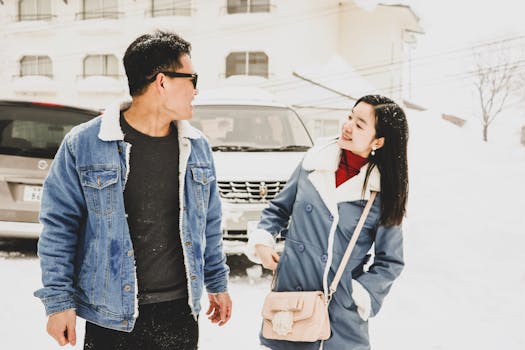 一对亚洲夫妇穿着温暖的冬装，在户外微笑着享受下雪的日子