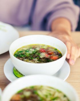 A warm, homemade vegetable soup in a white bowl on a wooden table, perfect for cozy dining moments.