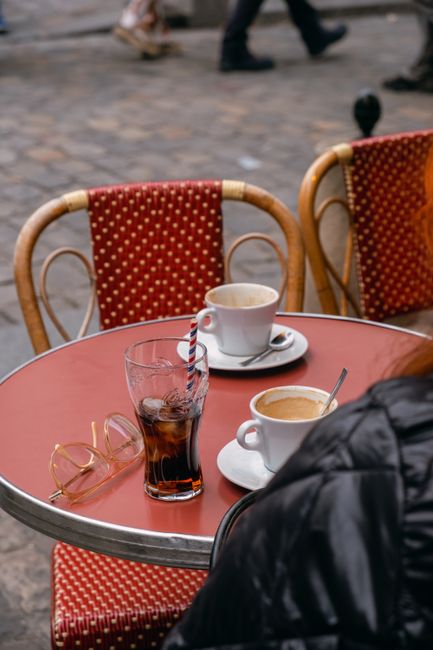 Charming outdoor café with coffee cups and a Coca-Cola glass on a red table, capturing street life.