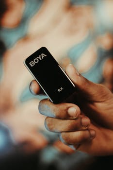 Detailed shot of a hand holding a BOYA wireless microphone indoors.