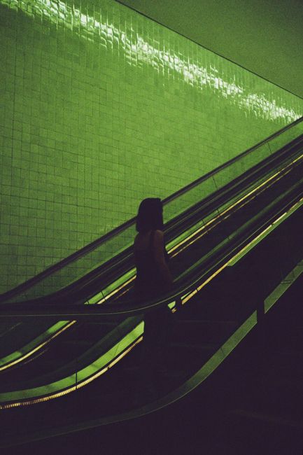 A mysterious silhouette of a woman on an escalator under green lighting, creating a cinematic atmosphere.