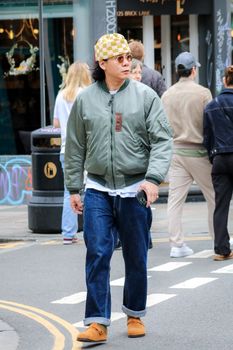 Fashionable man wearing sunglasses and a cap, walking on Brick Lane in London.