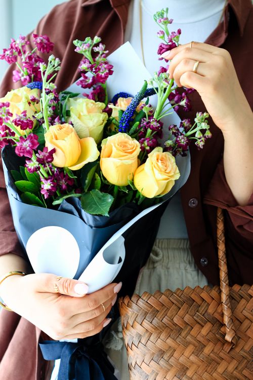 Free Close-up of a woman holding a colorful bouquet with yellow roses and purple flowers. Stock Photo