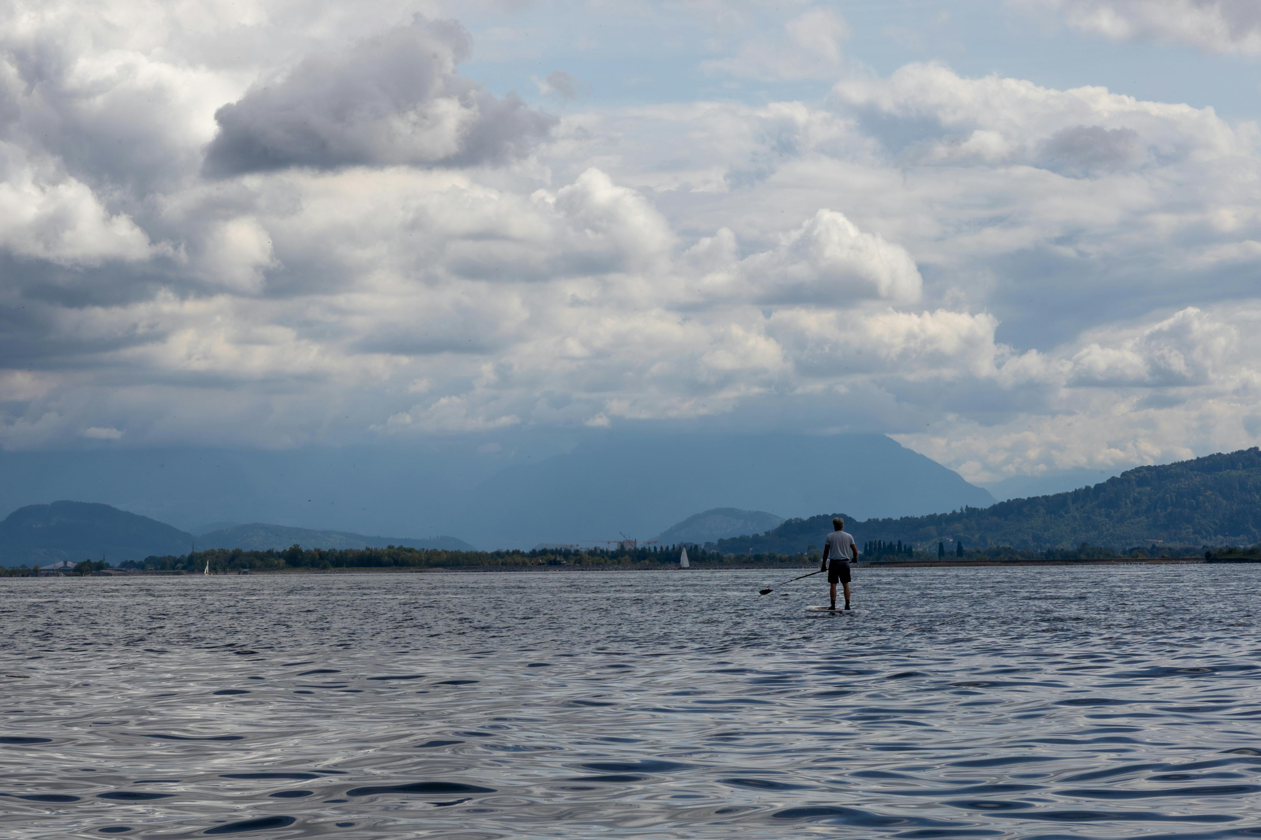 Person beim Stand up paddleboarding auf einem See mit Hügeln im Hintergrund