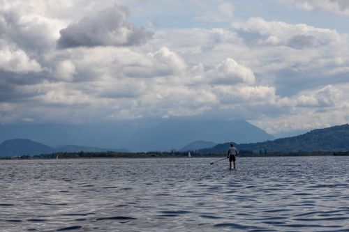 Free Paddleboarder enjoying a calm day on Lake Constance with scenic mountains and clouds. Stock Photo