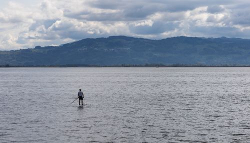 Free A man enjoys paddleboarding on a tranquil lake with scenic mountain views under a cloudy sky. Stock Photo