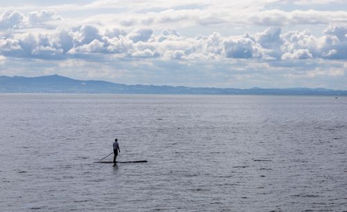 Free A serene paddle boarder on Lake Constance with mountains and a cloudy sky in the background. Stock Photo