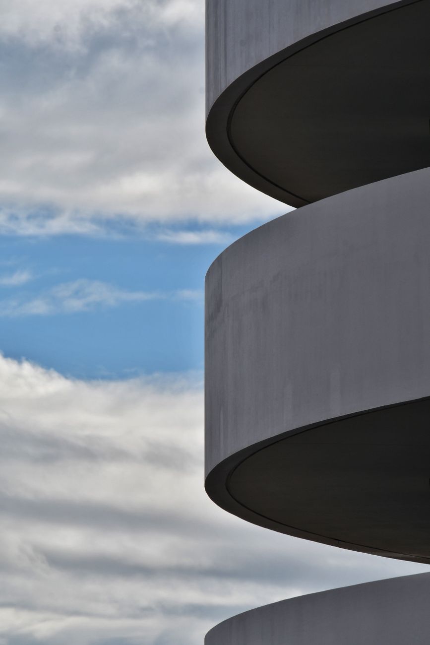 Minimalist view of modern architecture against a dramatic cloudy sky, creating an abstract composition.