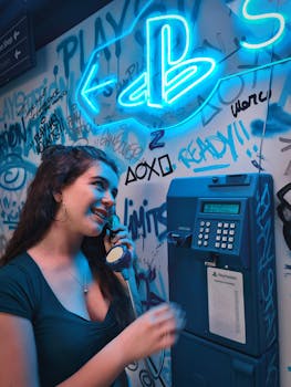 A woman interacts with a retro PlayStation-themed phone booth in a vibrant neon-lit room in Madrid.