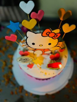 Vibrant Hello Kitty themed birthday cake with colorful decorations and a single lit candle, perfect for festive occasions.