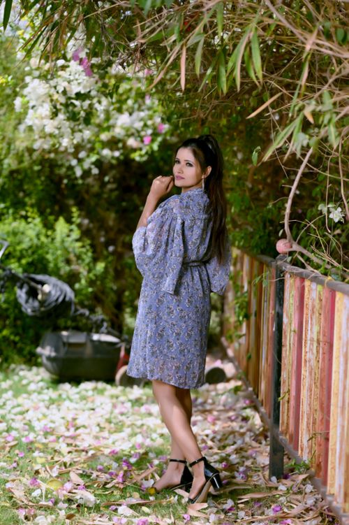 Free Fashionable woman in a blue floral dress poses outdoors surrounded by lush greenery. Stock Photo
