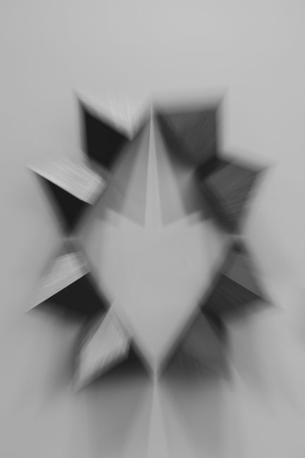 Blurred black and white geometric origami art with a grey background.