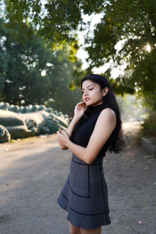 Free Fashion portrait of a young woman standing on a sunlit dirt road surrounded by trees. Stock Photo