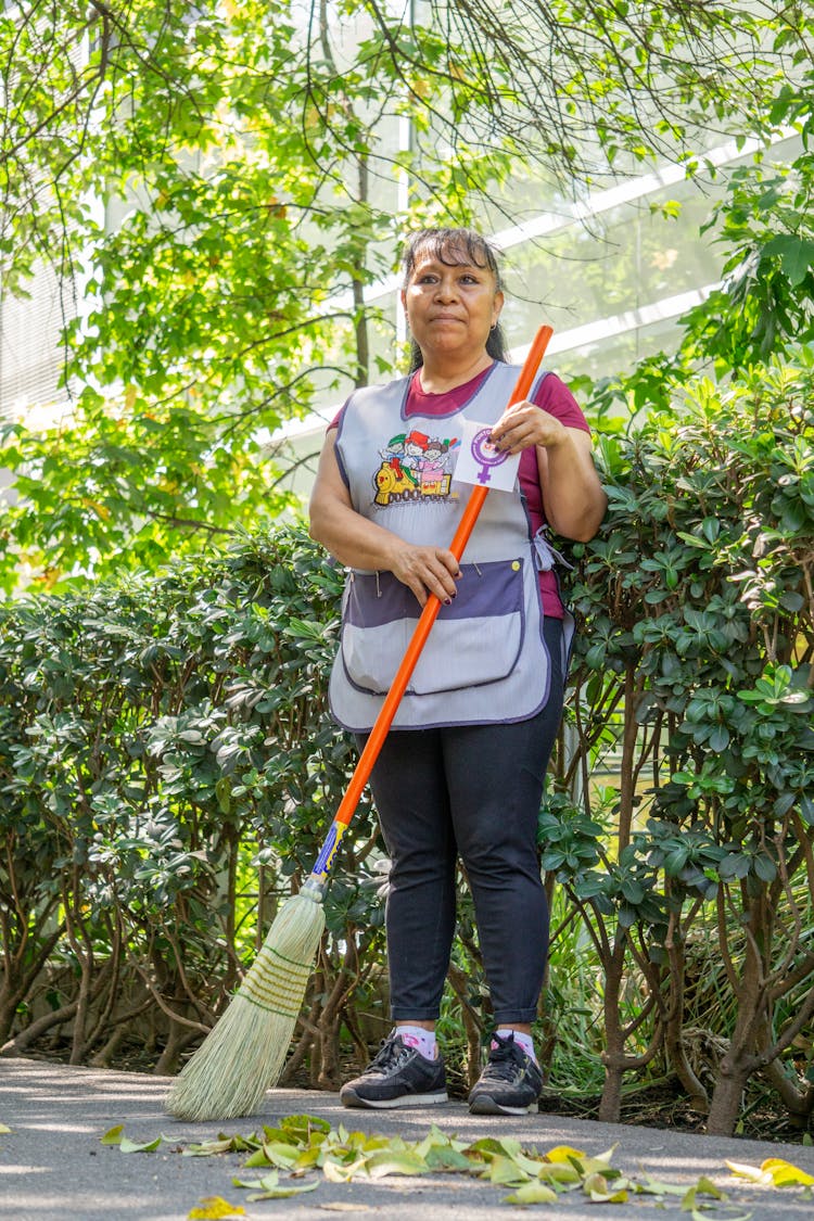 Photo Of A Senior Woman Sweeping Leaves On A Yard