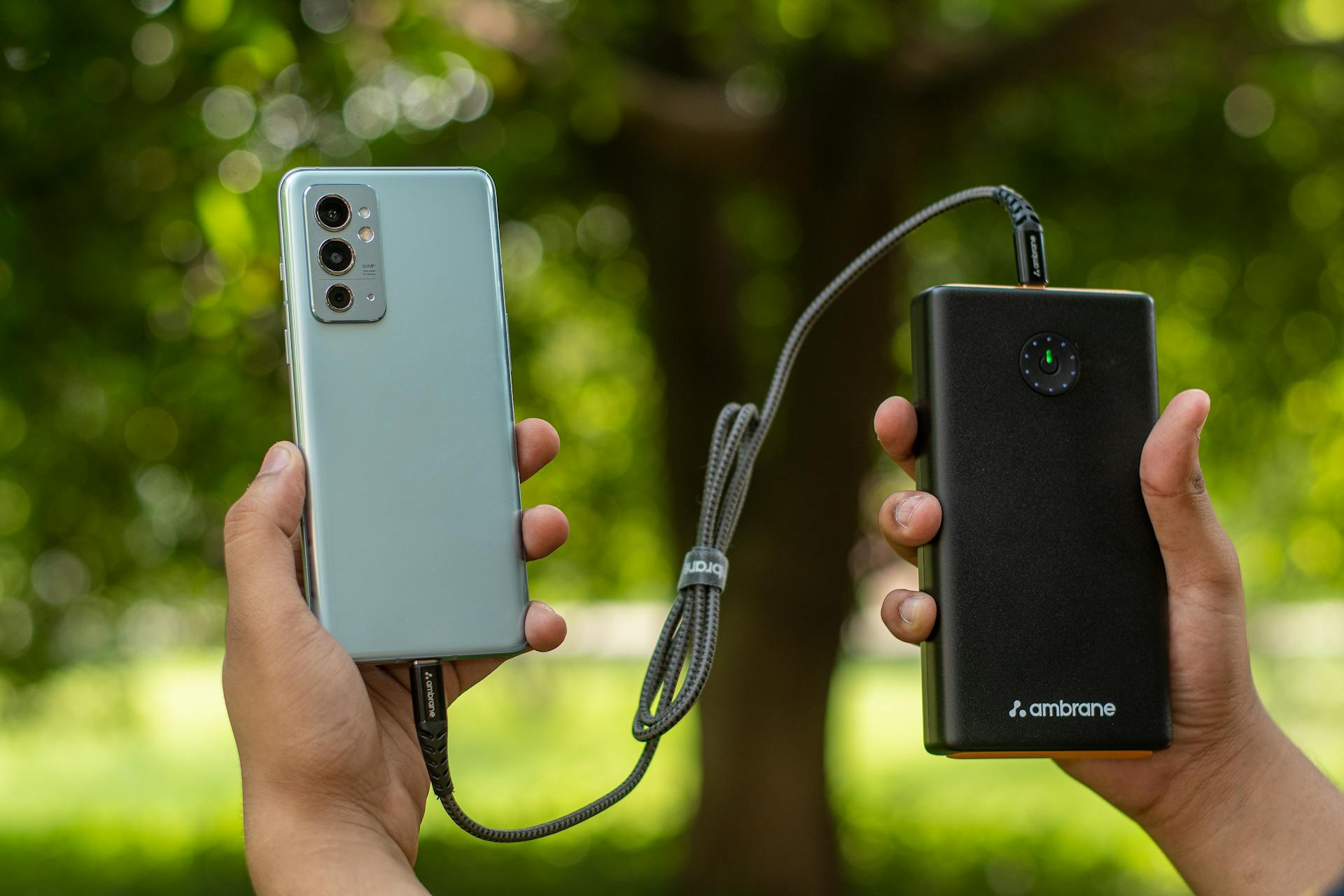 Close-up of hands holding a smartphone connected to a power bank outdoors.