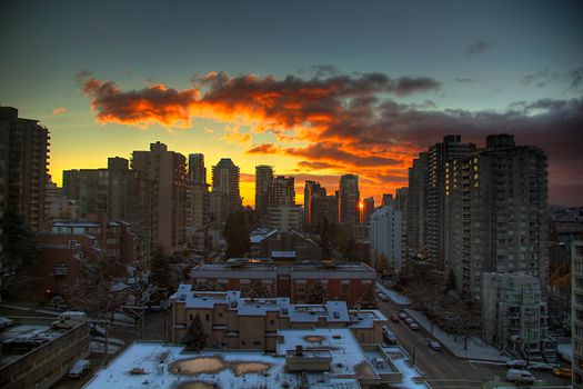 Breathtaking winter sunset over snowy urban skyline with high-rise buildings and vibrant clouds.