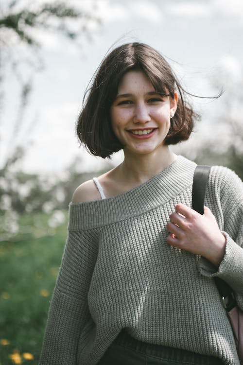 Photo of a Smiling Girl Wearing a Grey Sweater in a Park