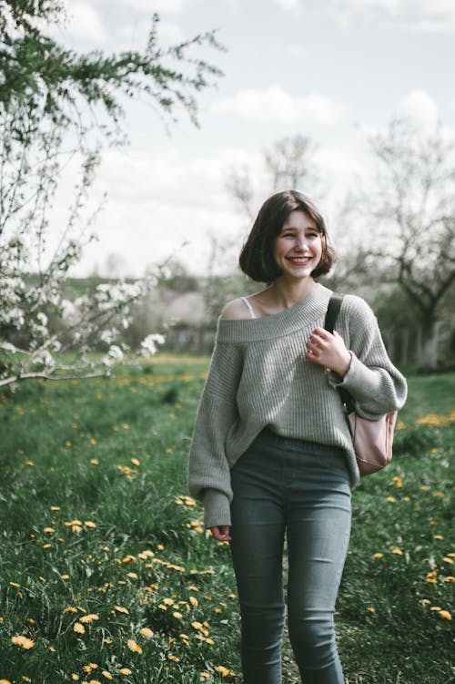 Photo of a Smiling Girl Wearing a Grey Sweater Standing in a Park