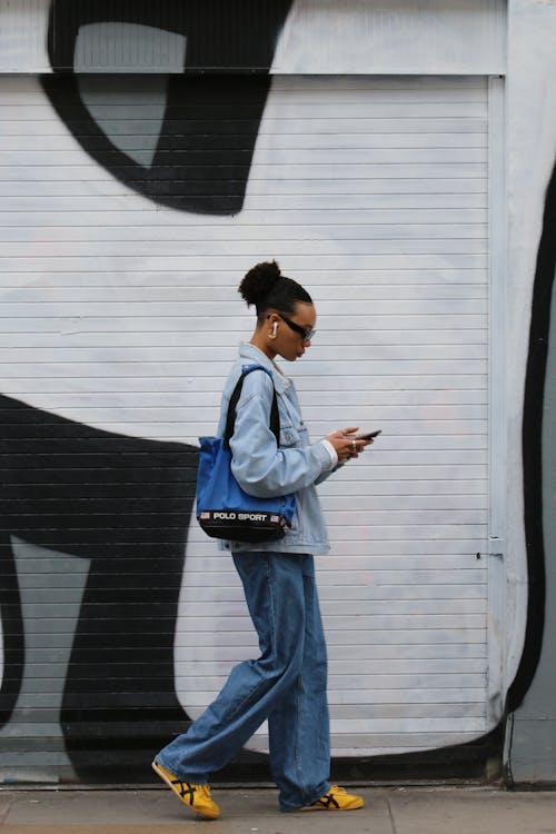 Side View of a Woman Walking with a Phone by a Wall with a Mural