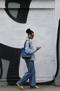 Woman in casual clothing walking past a mural in London while using a phone.