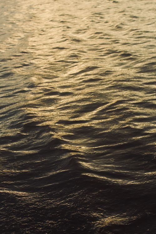 Free Sunlit ocean waves creating a warm, abstract texture at sunset. Stock Photo