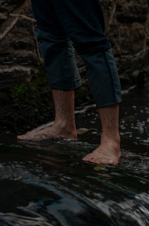 Dark Photo of a Man Standing Barefoot in a Stream