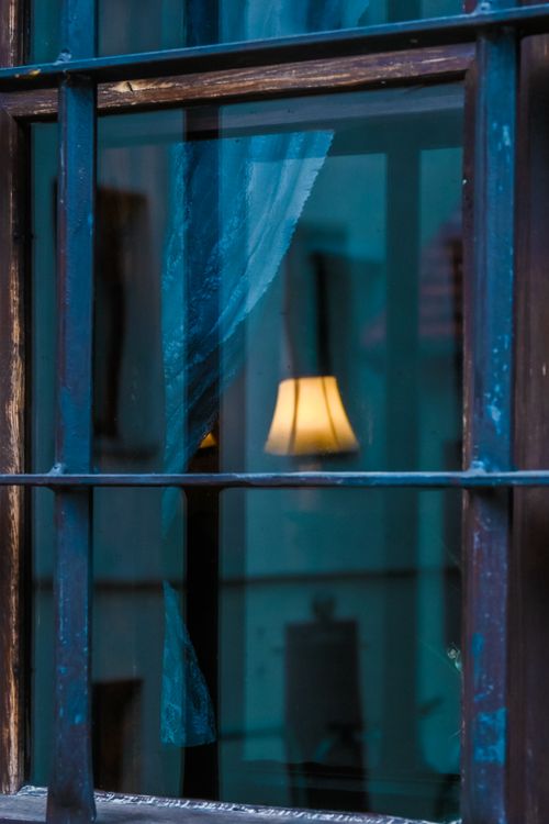 Free A retro-style lamp reflecting through a barred window with a blue curtain. Stock Photo