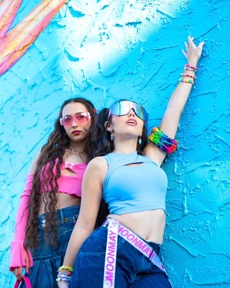 Girls In Bright Outfits And Sunglasses Posing Near Blue Wall