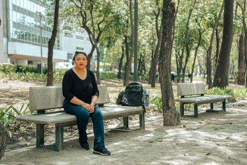 Free Woman sitting on a bench in an urban park surrounded by trees, daylight. Stock Photo