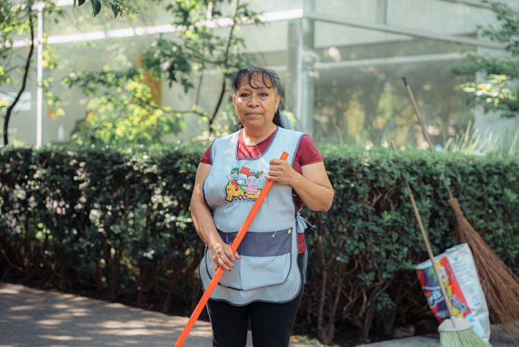 Woman In Uniform Sweeping Street With Brush