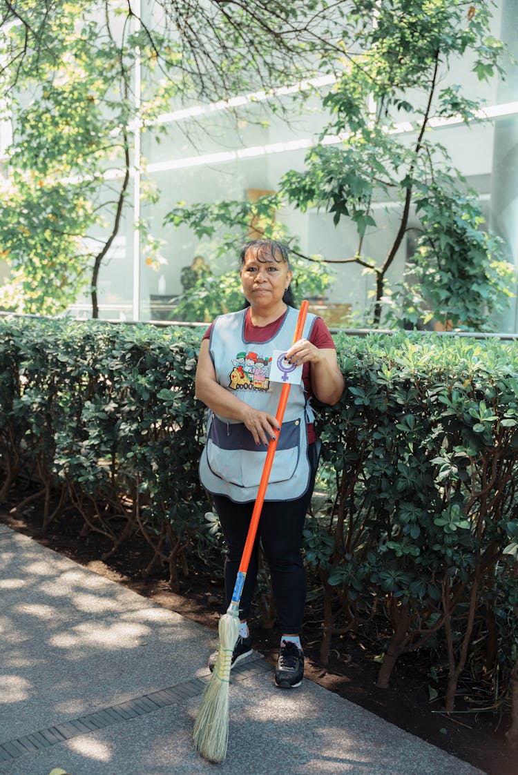 Woman In Uniform Sweeping Street With Brush