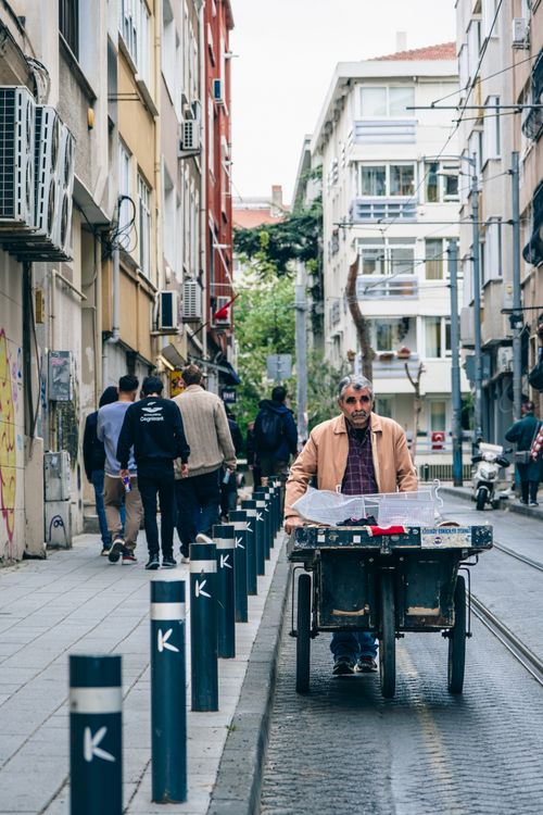 Free Senior man pushing a cart down a bustling city street with residential buildings and pedestrians. Stock Photo