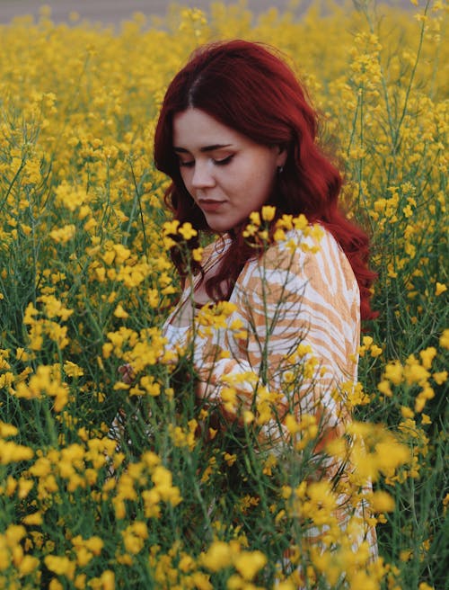 Young Woman with Red Hair Standing on a Field with Yellow Flowers