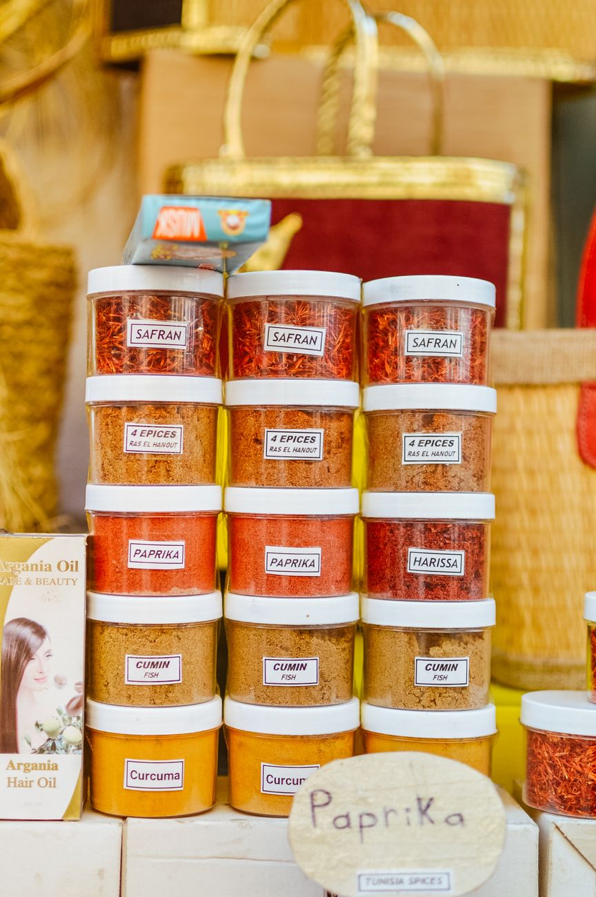 Bowl of red harissa paste surrounded by dried chiles, garlic, and whole spices on a wooden surface