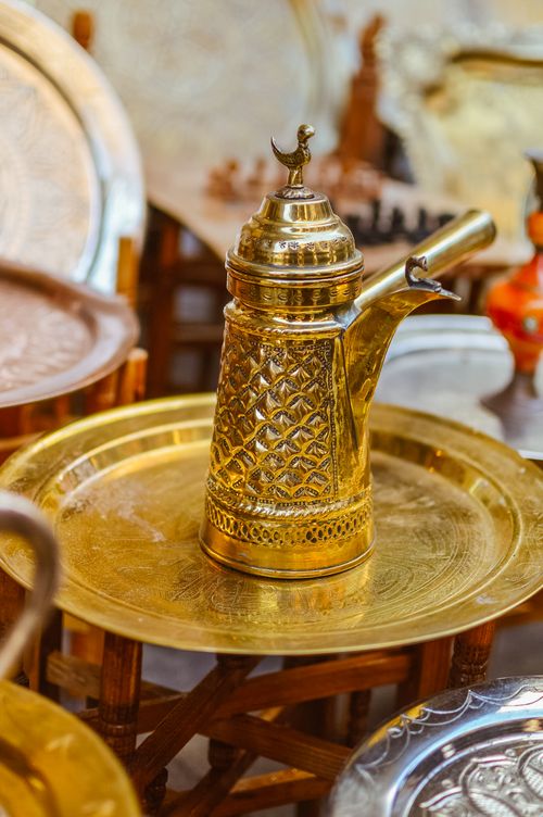 Free Traditional brass pitcher with intricate patterns on a decorative gold tray, in a market setting. Stock Photo