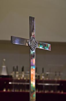 Close-up of a silver cross with colorful reflections in a church setting.
