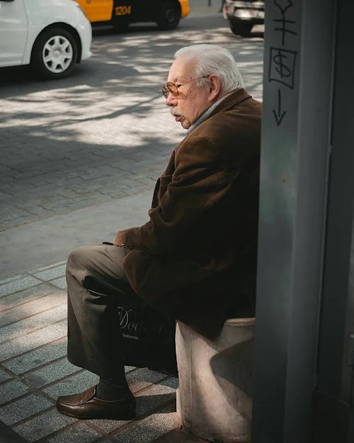 Elderly Man Sitting on Wall on Sidewalk