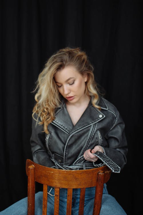 Young Model Tying the Belt of Her Leather Jacket Sitting Backward on the Chair
