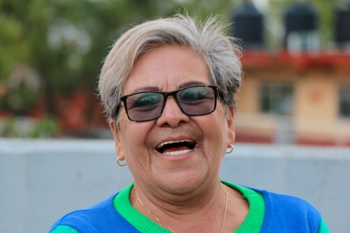 Free Portrait of a laughing senior woman wearing sunglasses and a blue top, enjoying a sunny day outdoors. Stock Photo