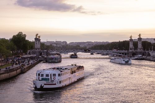 Free Scenic sunset view of the Pont Alexandre III over the Seine River with boats and vibrant Paris skyline. Stock Photo