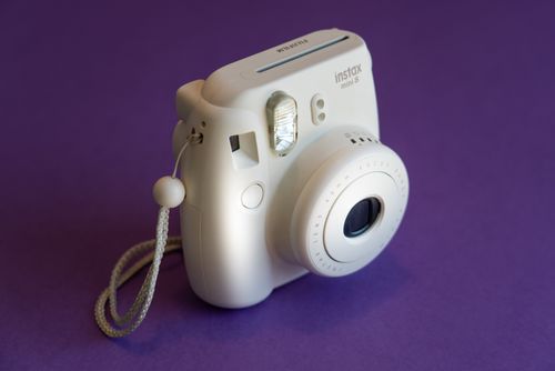 Free White Fujifilm Instax Mini 8 camera displayed against a vibrant purple backdrop. Stock Photo