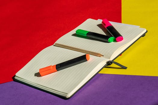 Highlighters and pencil on a notebook with colorful paper background.