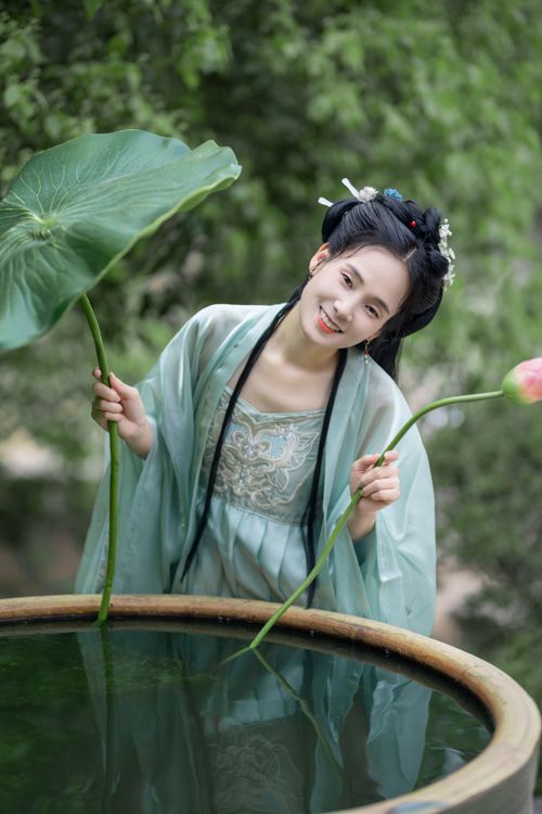Free Woman in traditional attire with lotus leaves by a serene pond in a garden setting. Stock Photo