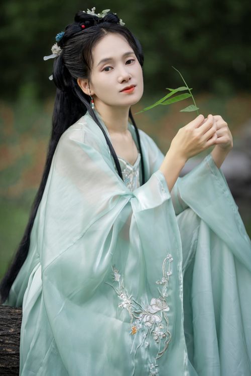 Free A woman in traditional Chinese dress sits outdoors, holding a leaf, exuding grace and tranquility. Stock Photo
