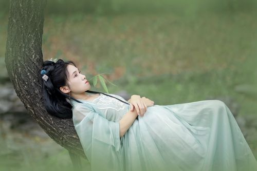 Free A woman in traditional Asian attire reclining against a tree, exuding tranquility outdoors. Stock Photo