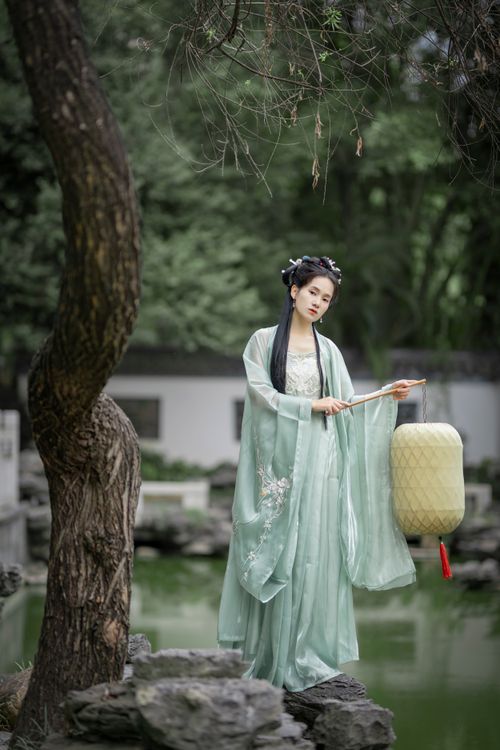 Free Woman in traditional attire holding a lantern in a serene garden setting. Stock Photo